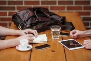 Two people sitting at wooden table with iphones and ipad, coffee and water.