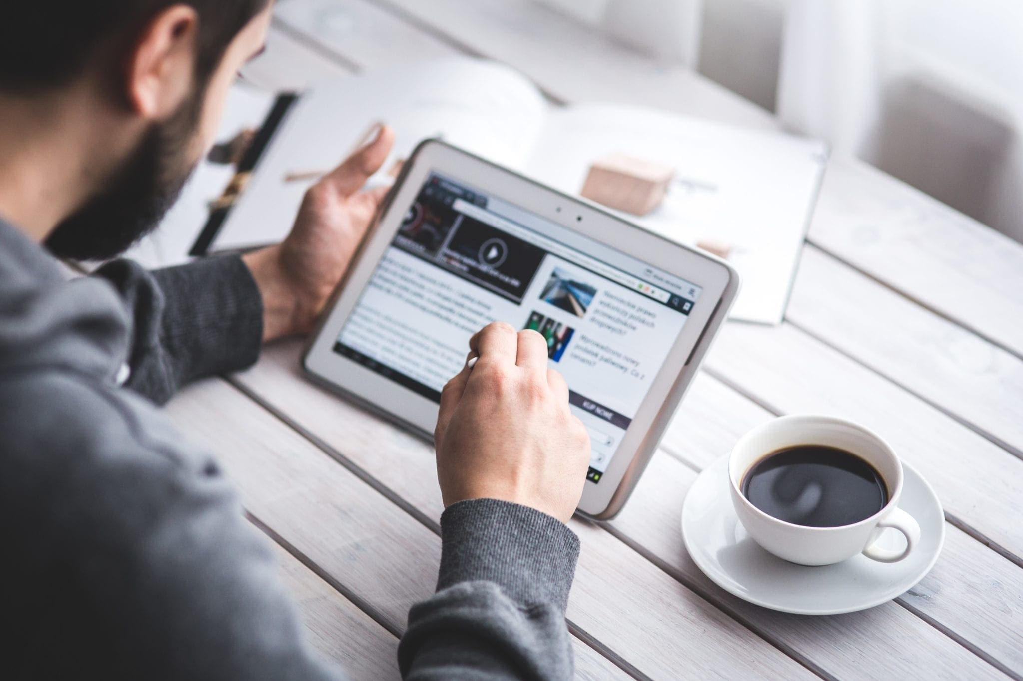 Man sitting at table holding a tablet and cup of coffee.